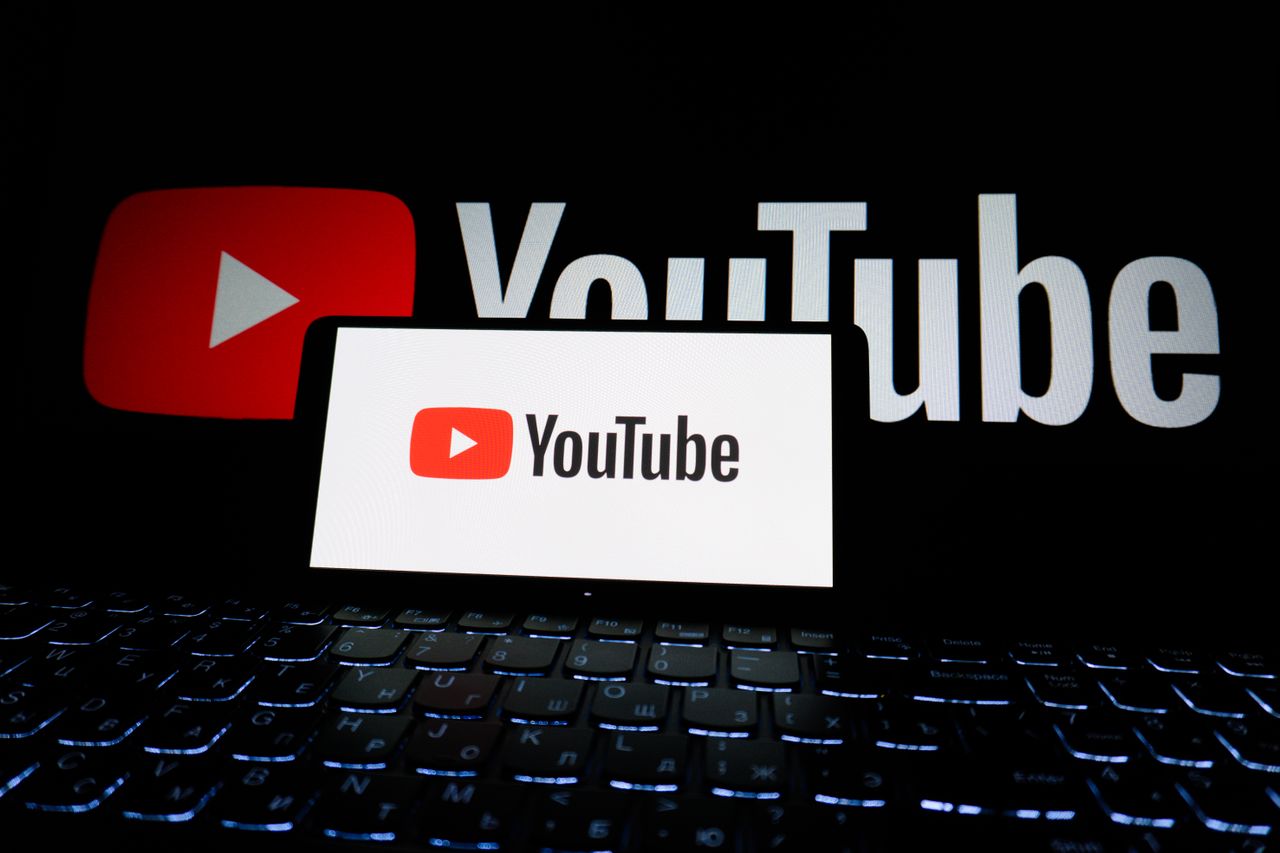 A close-up view of the YouTube logo shown on a laptop screen in a dimly lit setting.